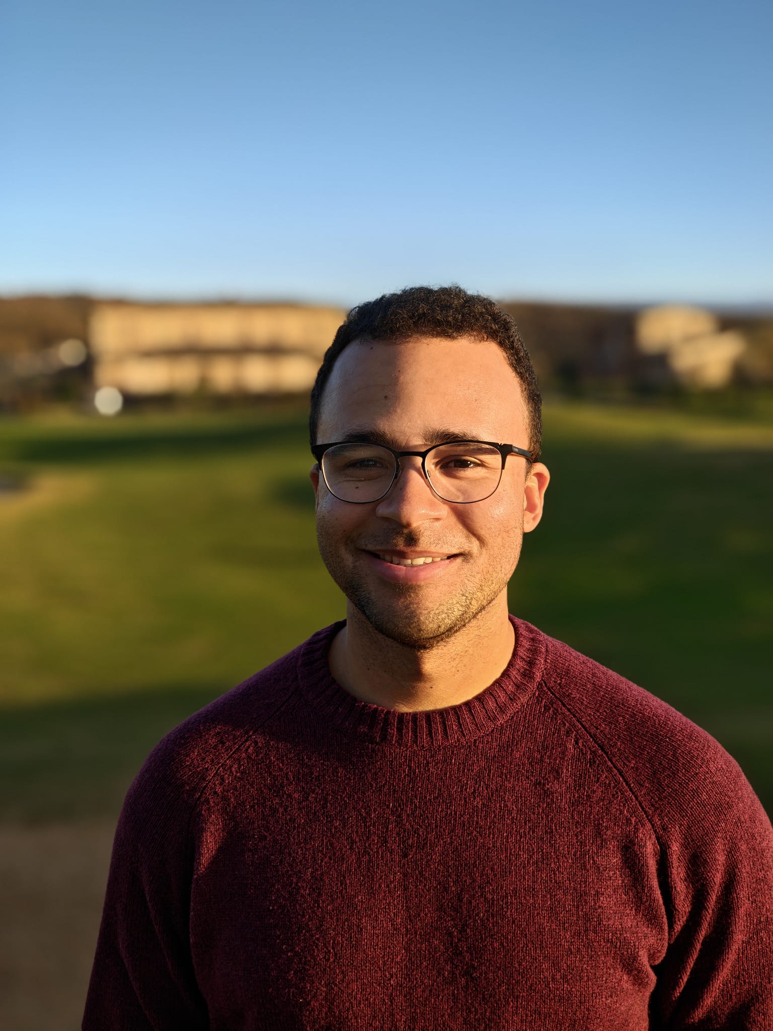 A picture of the websites creator smiling with a red sweater on and glasses